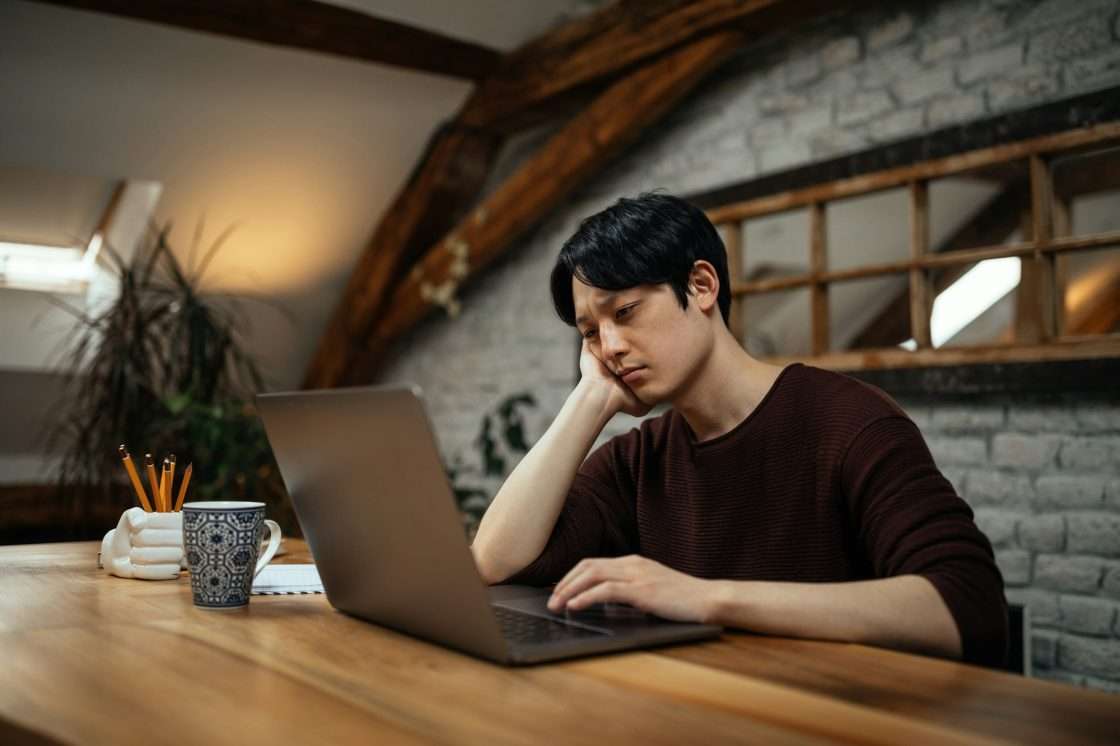 Worried japanese man working at home via laptop